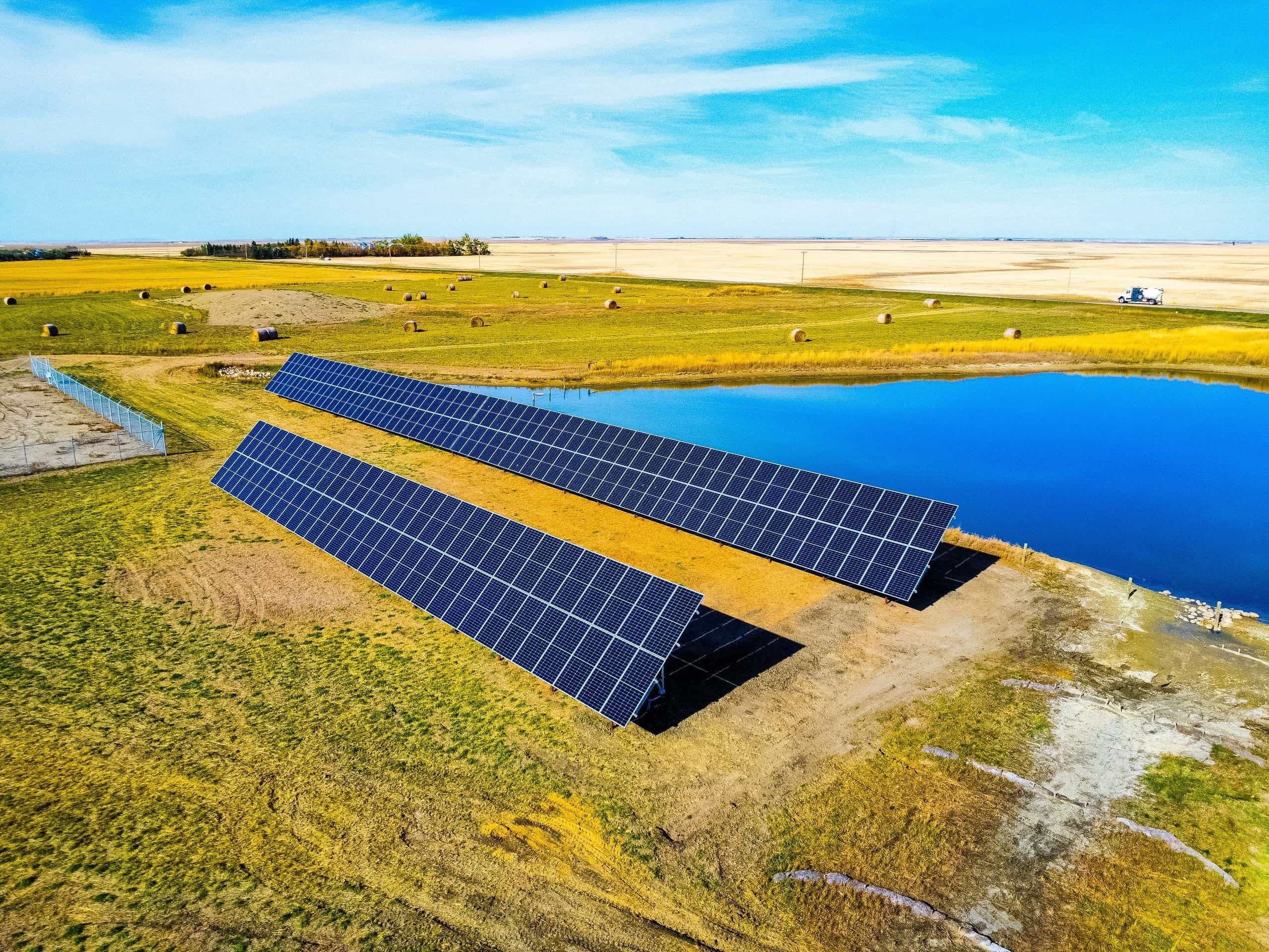 Aerial view of two rows of ground-mount solar panels beside the retention pond at the SaskEnergy site, farmland beyond