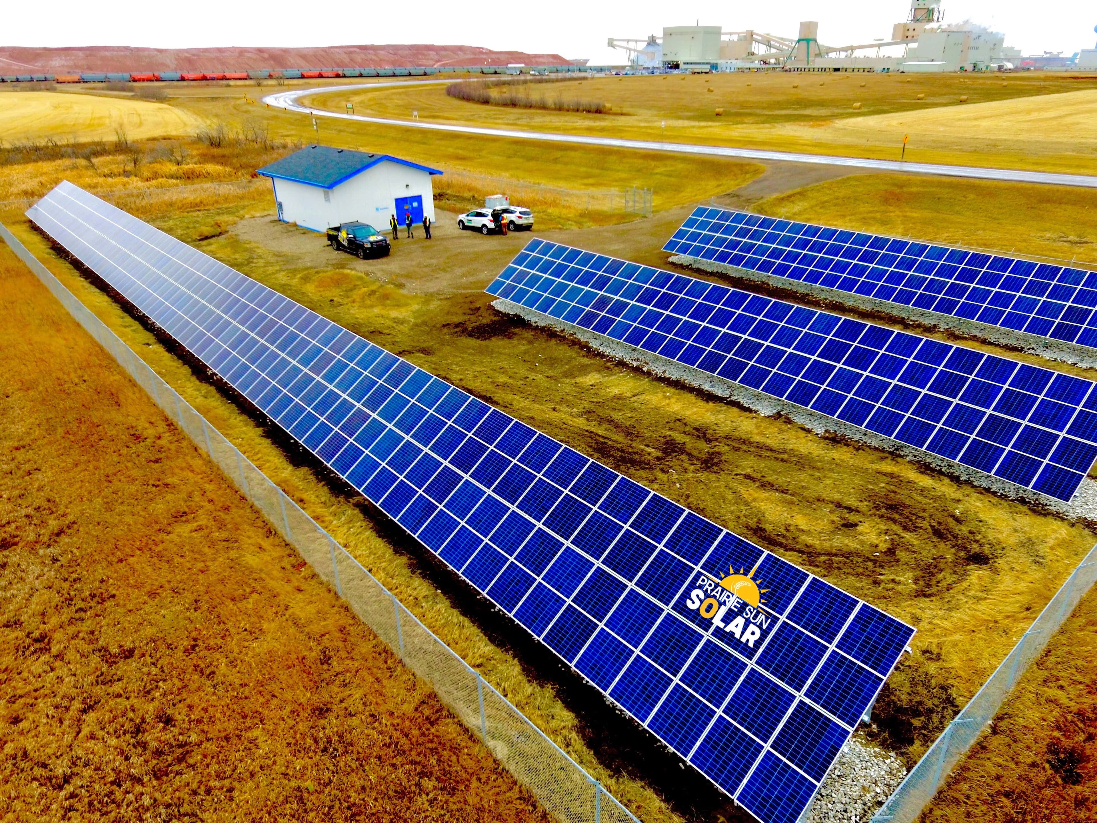 Aerial view of four rows of ground-mount solar panels beside the SaskWater Cory Booster Station west of Saskatoon