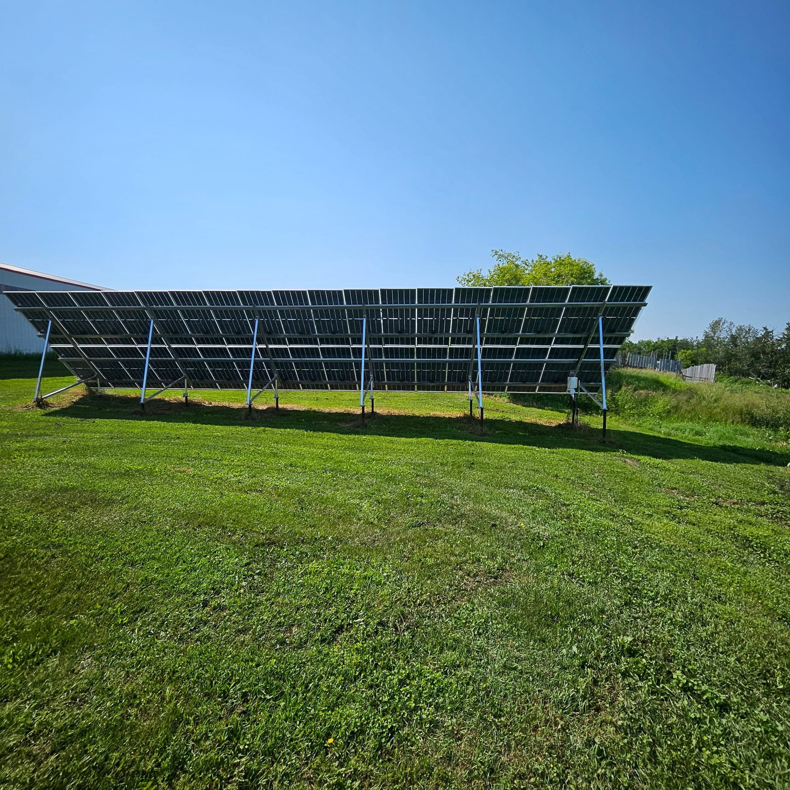 The Badinski ground-mount solar array seen end-on across mown grass, with a treeline behind